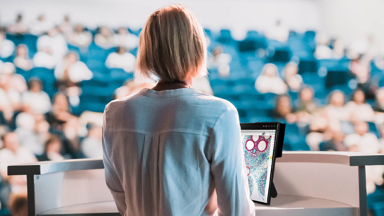 Back view of a professional speaker using the SMART Board Mini Interactive Podium for a presentation in front of a seated audience.