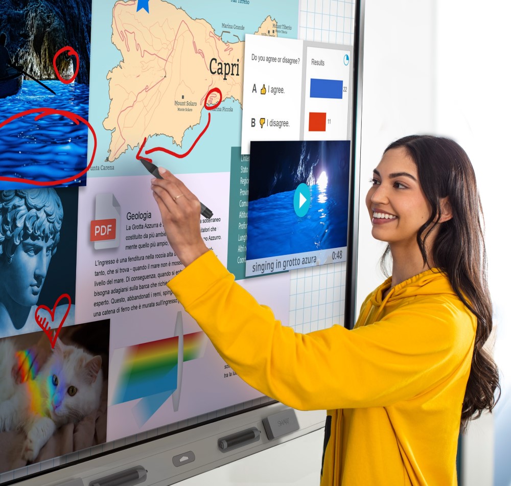 Teacher in a yellow jacket interacts with a SMART board displaying a colorful map for a geography lesson.